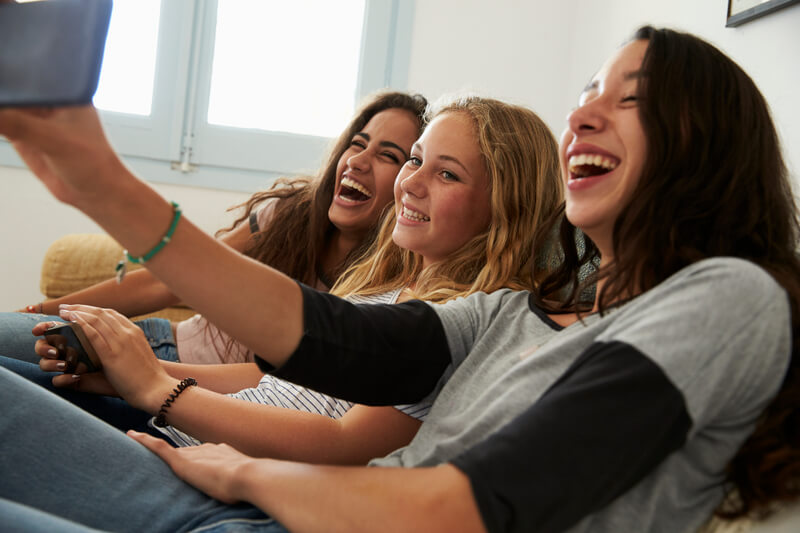 Teenage girl taking selfie with friends using her smartphone