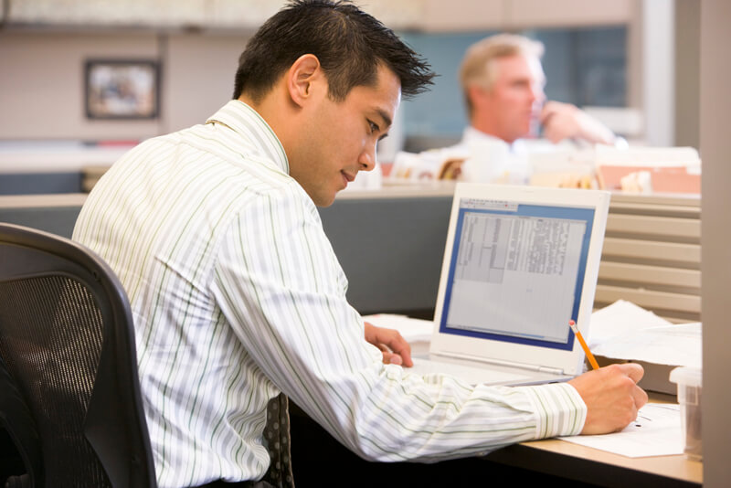 Businessman in cubicle with laptop writing